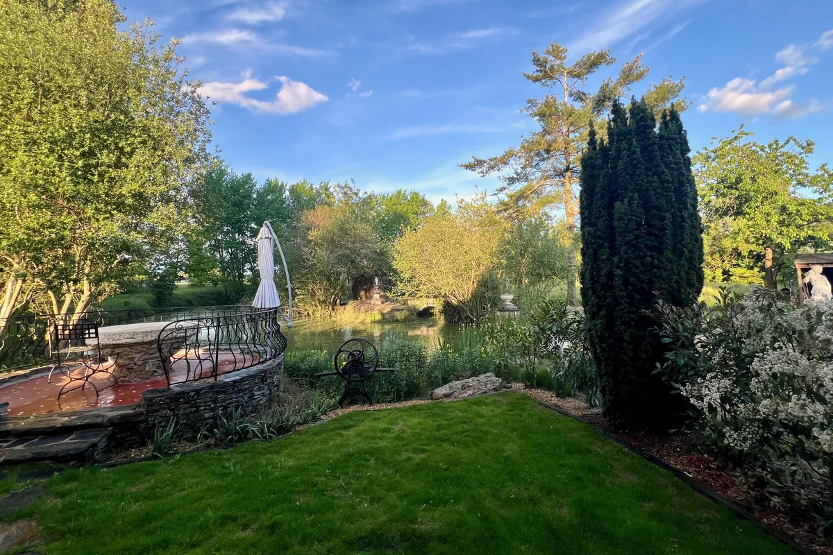 La mare du jardin bordée d’arbres et de massifs fleuris, à Corné